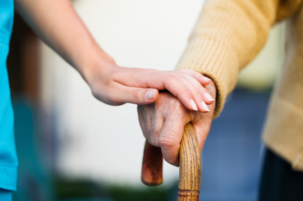 hand on elderly hand holding cane